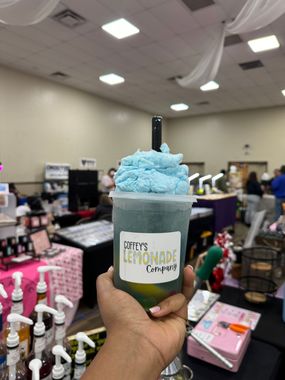 A person is holding a cup of lemonade with cotton candy on top.