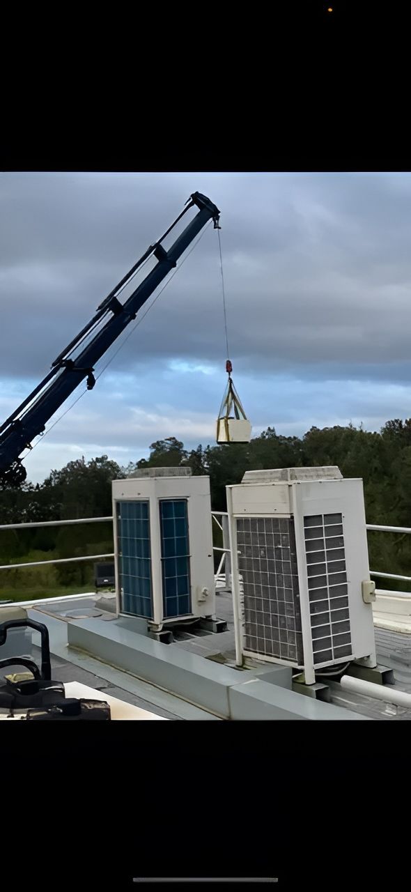 A Crane Lifting An Object Onto A Rooftop — Refrigeration & Air Conditioning in Jewells, NSW