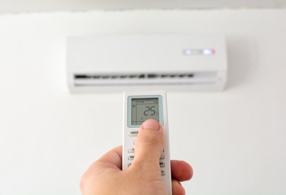 Hand With Remote Control Directed on The Conditioner — Refrigeration & Air Conditioning in Jewells, NSW
