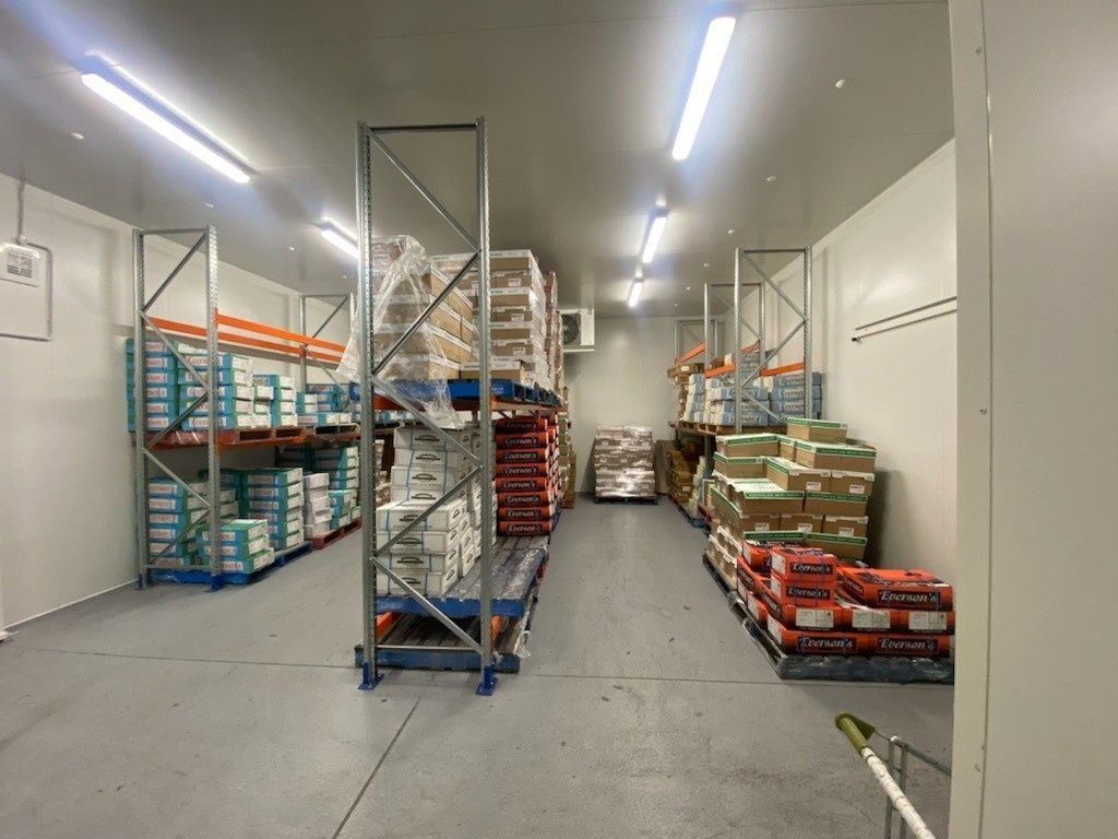 Warehouse Interior with Shelves of Packaged Goods on Pallets Under Bright Lights — Refrigeration & Air Conditioning in Jewells, NSW