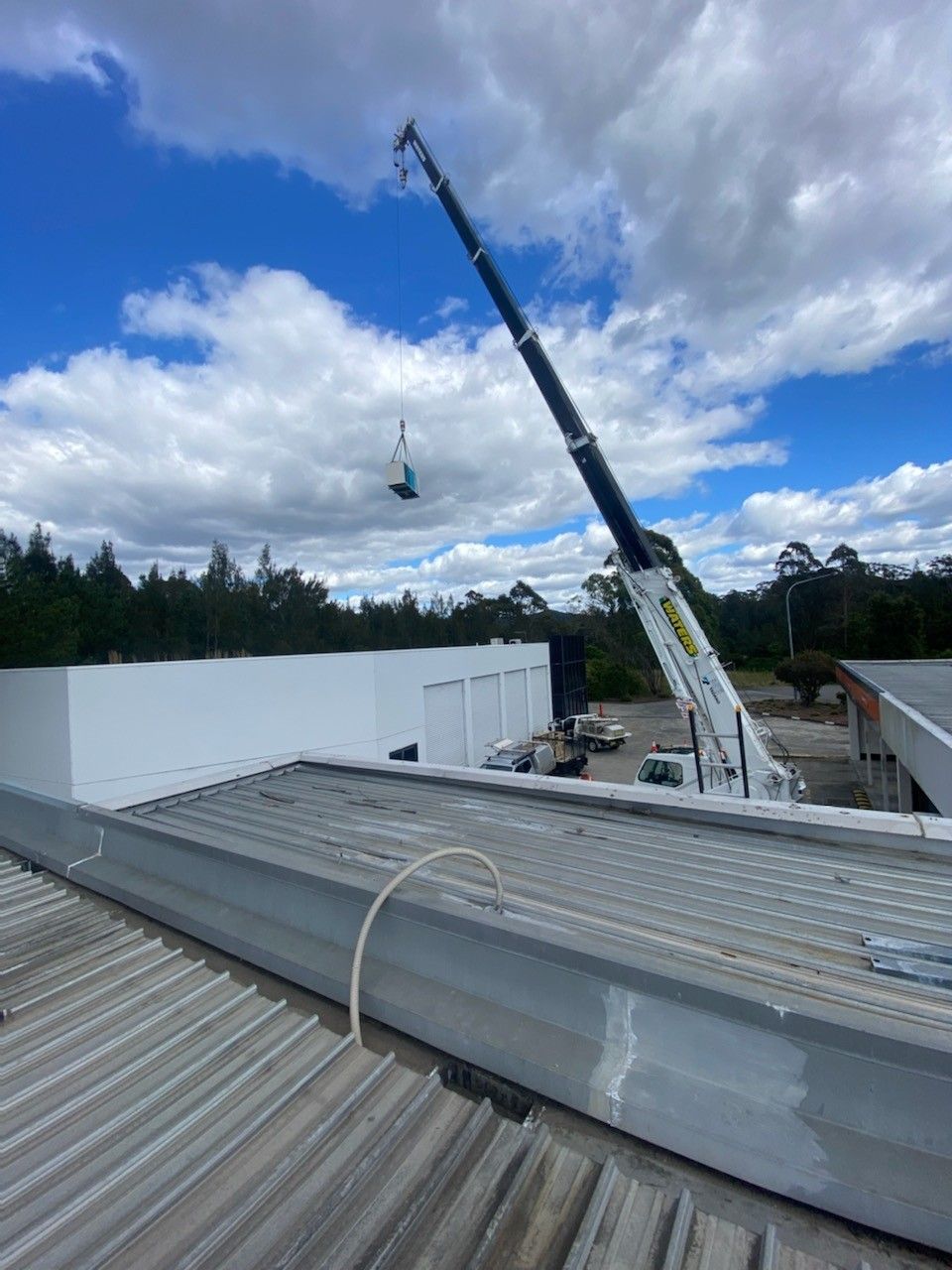 A Crane Lifting an Object Over a Building with A Cloudy Sky in The Background — Refrigeration & Air Conditioning in Maitland, NSW