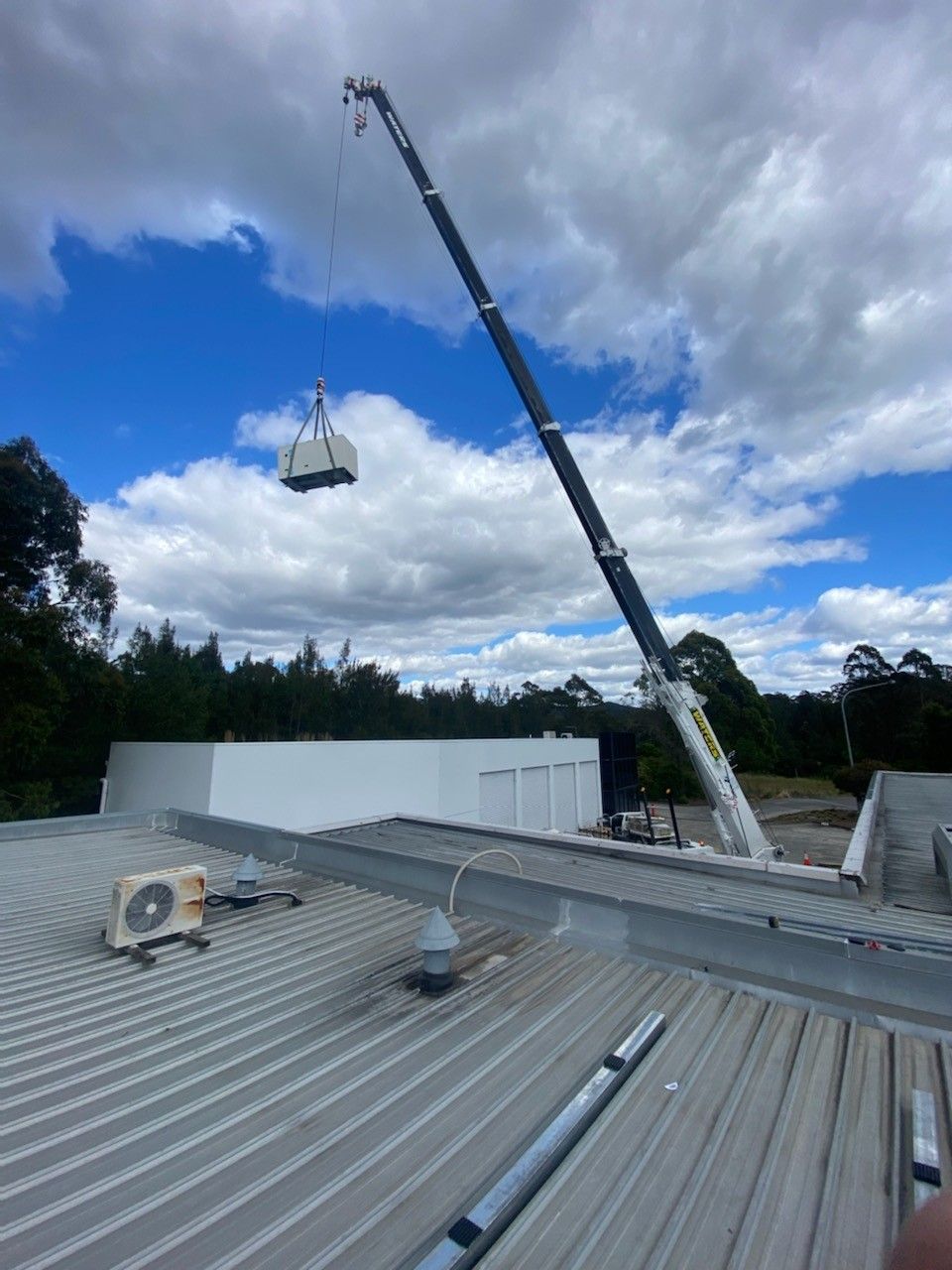 A Crane Lifting a White Rectangular Object onto A White Roof on A Cloudy Day — Refrigeration & Air Conditioning in New Castle, NSW