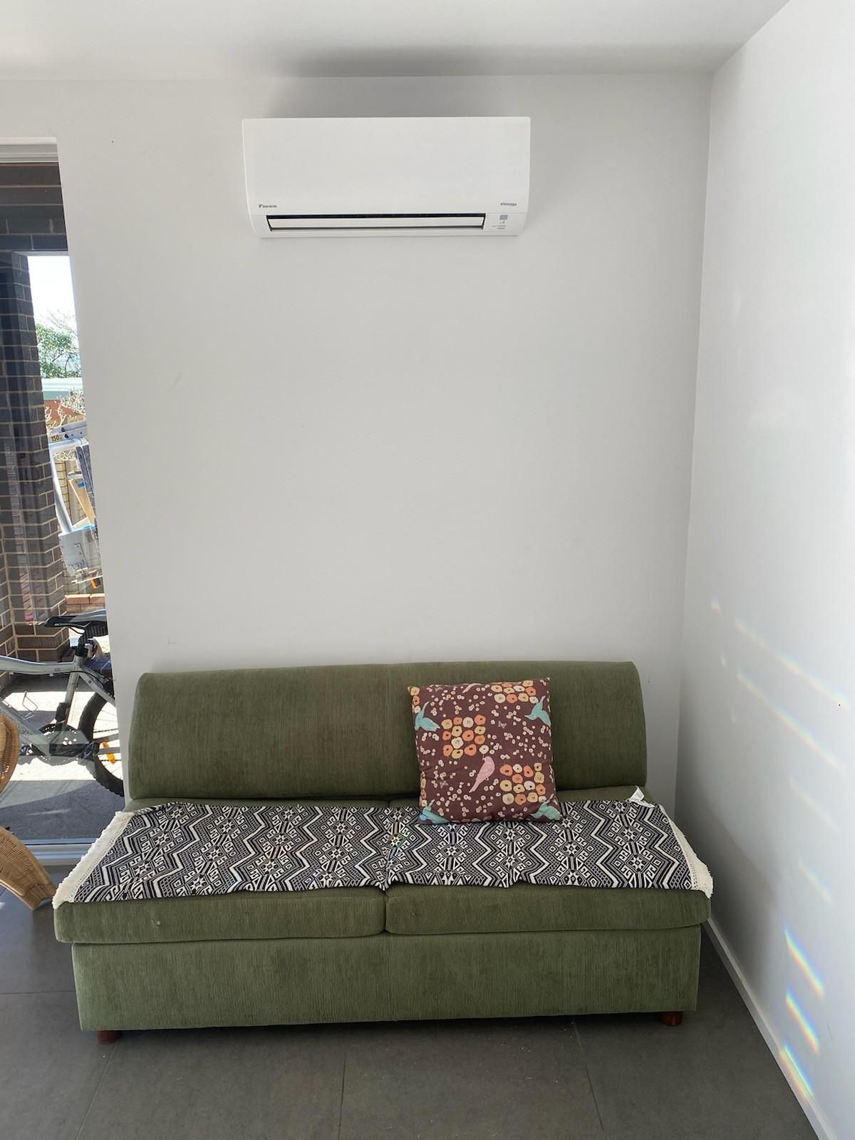 Green Sofa with Patterned Cushion, Below a White Air Conditioner — Refrigeration & Air Conditioning in Central Coast, NSW