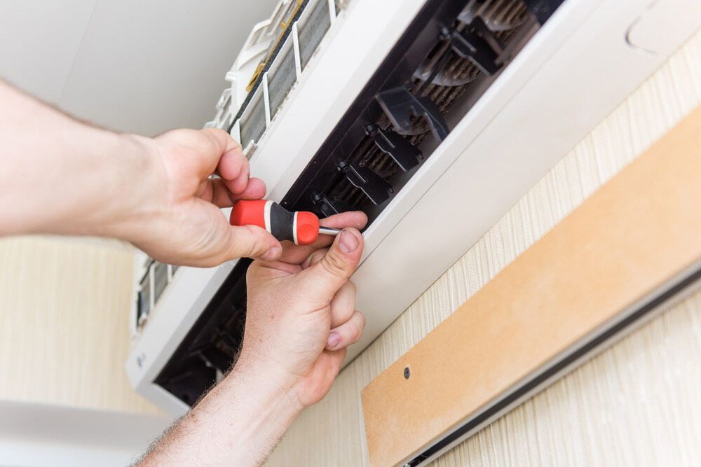 Person Using a Screwdriver to Repair a White Air Conditioner — Refrigeration & Air Conditioning in Port Stephens, NSW