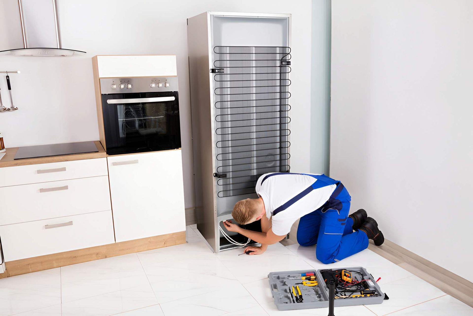 Repairman Kneeling, Working on the Back of a Refrigerator — Refrigeration & Air Conditioning in Maitland, NSW