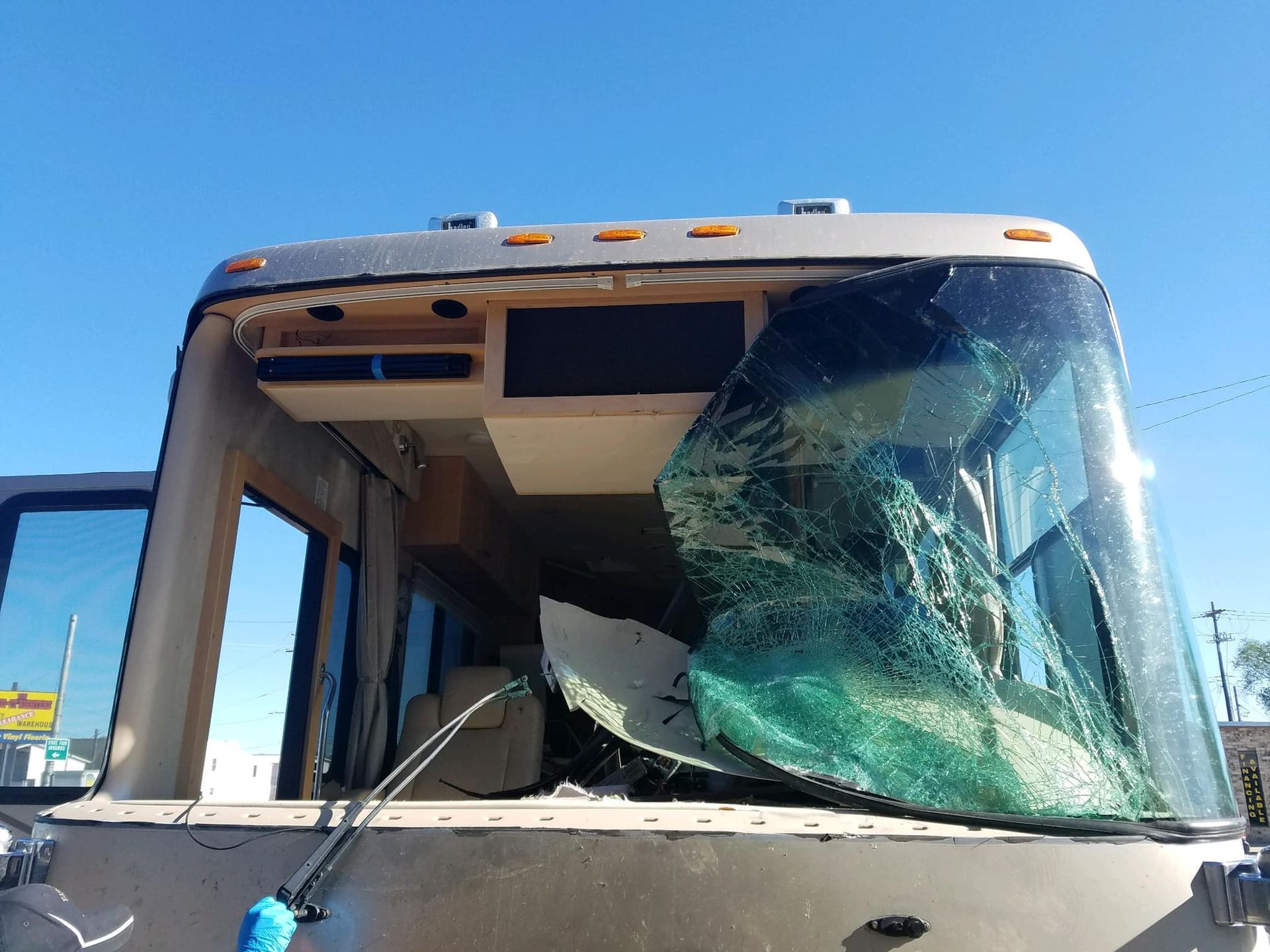 RV with a shattered windshield, beige exterior, under a clear, blue sky.
