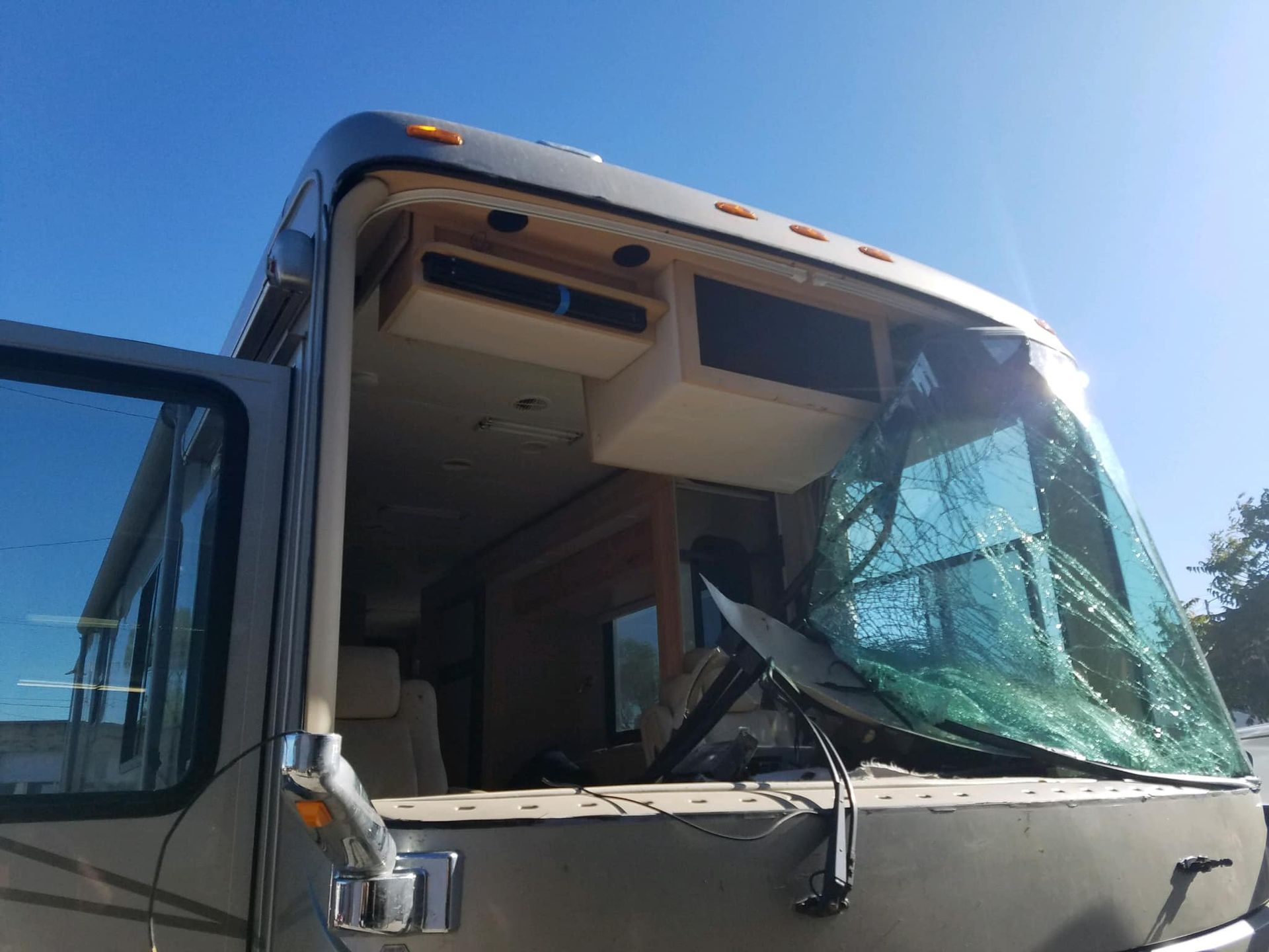 RV with shattered windshield and open driver's side door, against a bright blue sky.