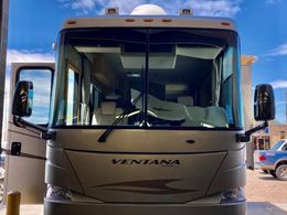 Tan Ventana motorhome parked, door open, reflecting blue sky and building in windows.