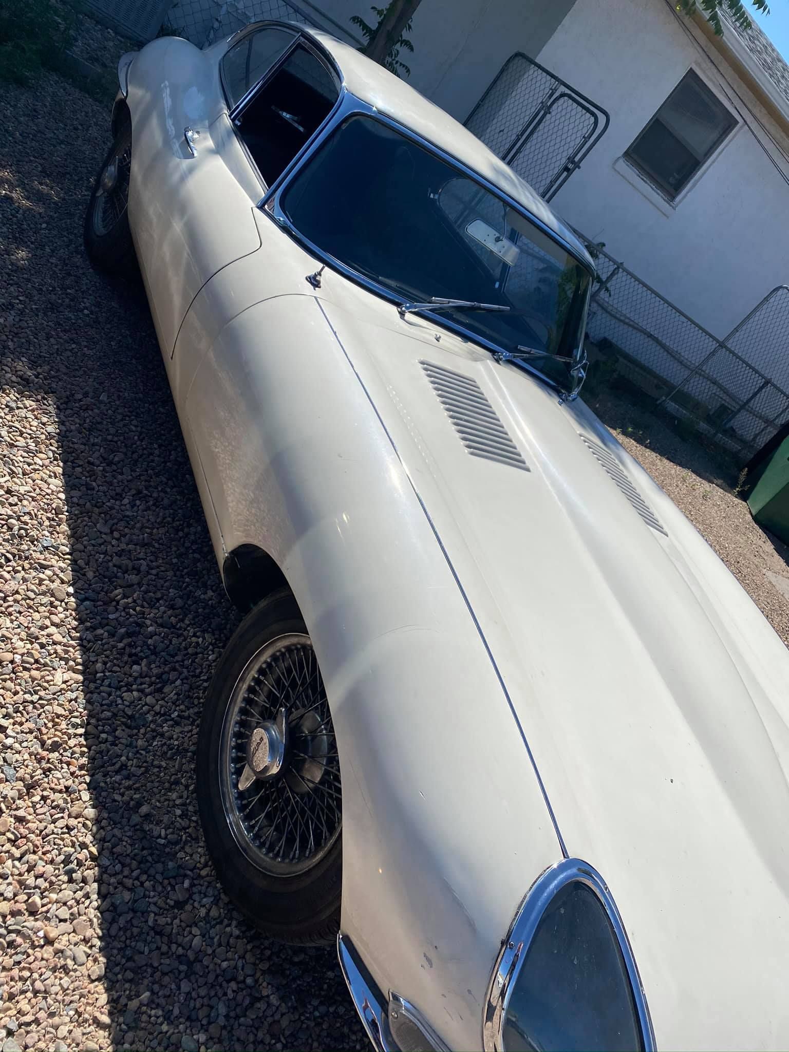 White classic Jaguar E-Type car parked on gravel, sunny day.