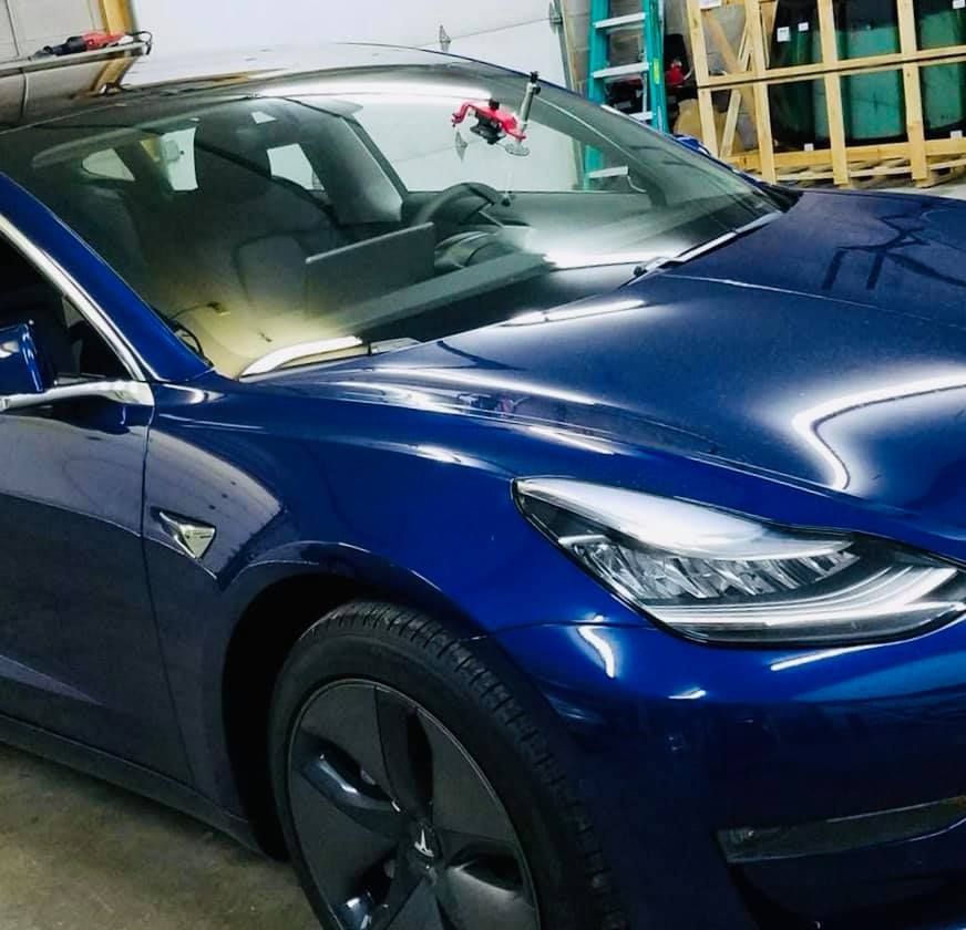 Blue Tesla car parked indoors, reflecting bright lighting.
