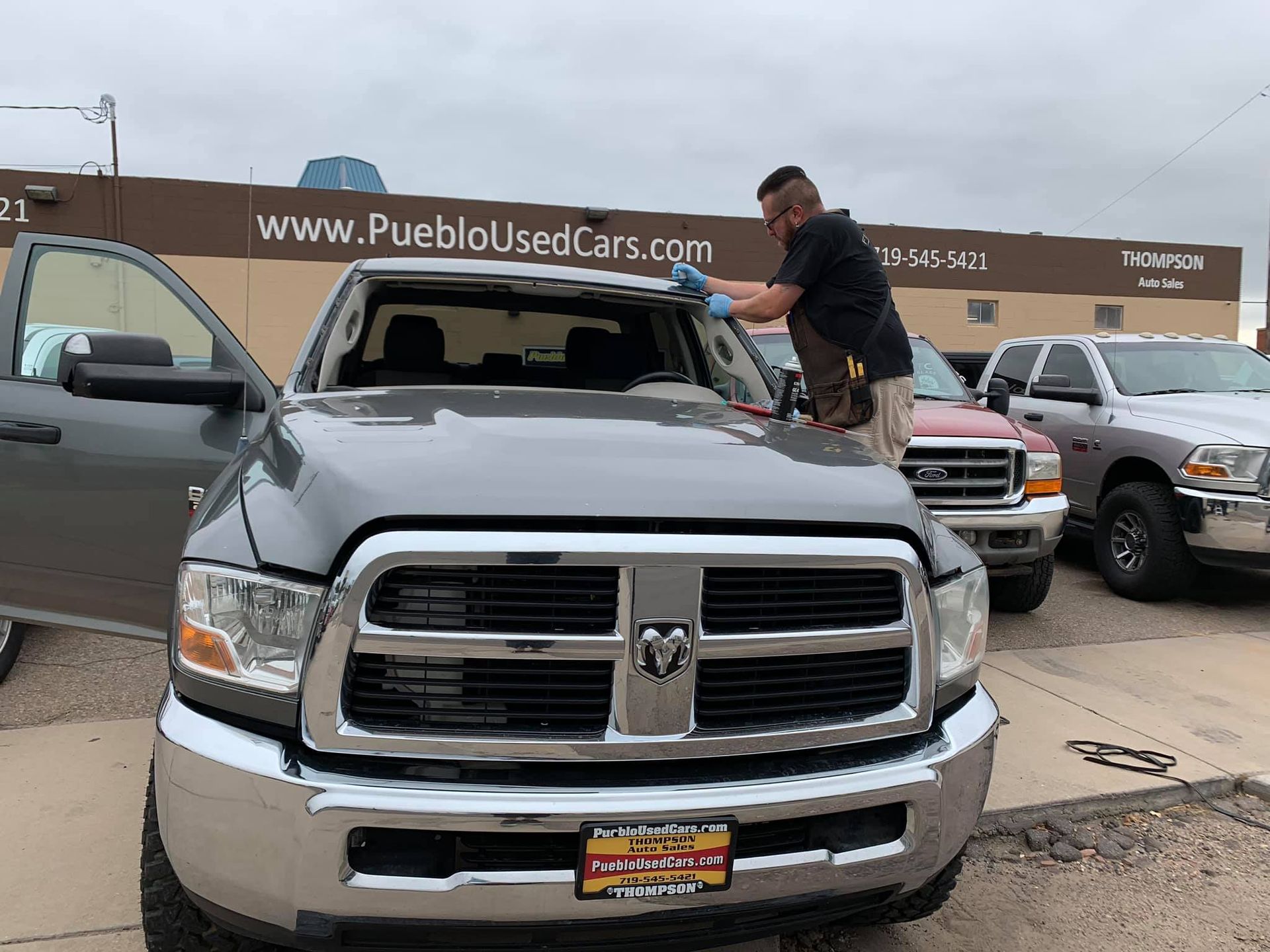 Man replacing windshield on a gray Dodge Ram truck in front of