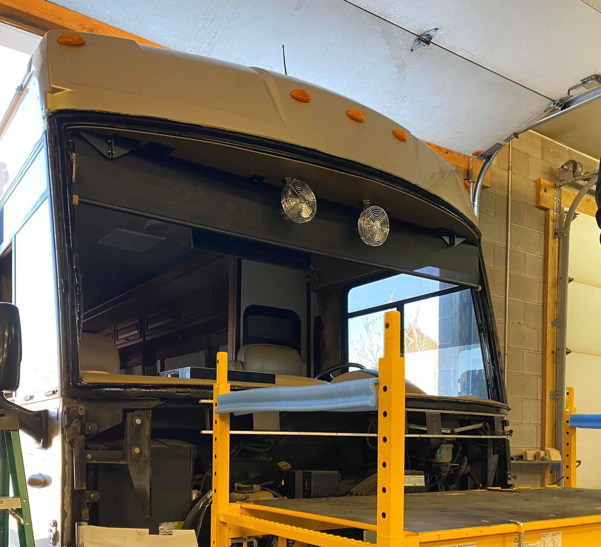 RV front with windshield removed, surrounded by scaffolding, in a garage.