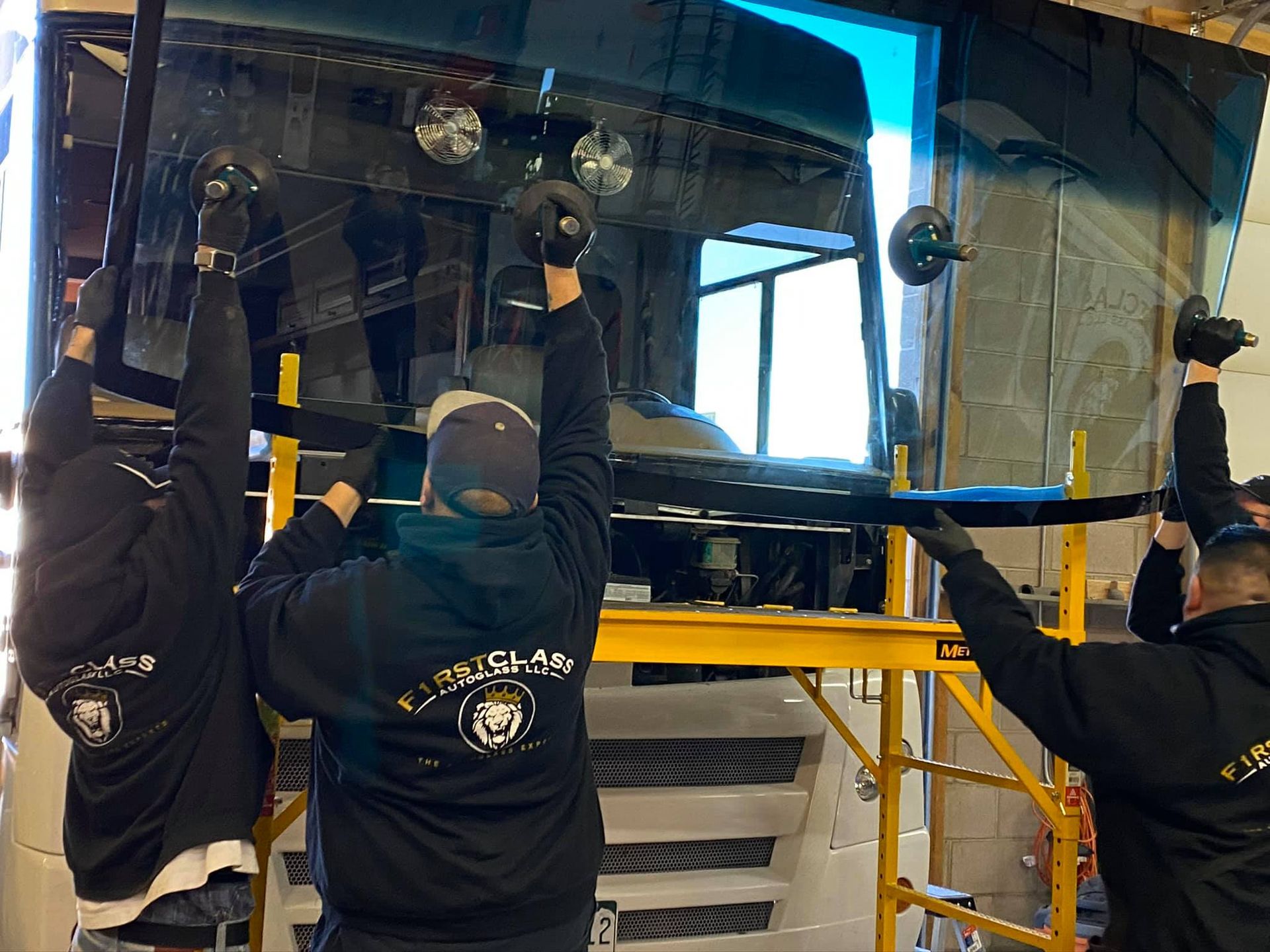 Three workers installing a large pane of glass, using suction cups, in a workshop setting.