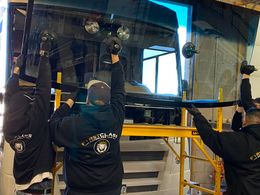 Three workers installing a large pane of glass, using suction cups, in a workshop setting.