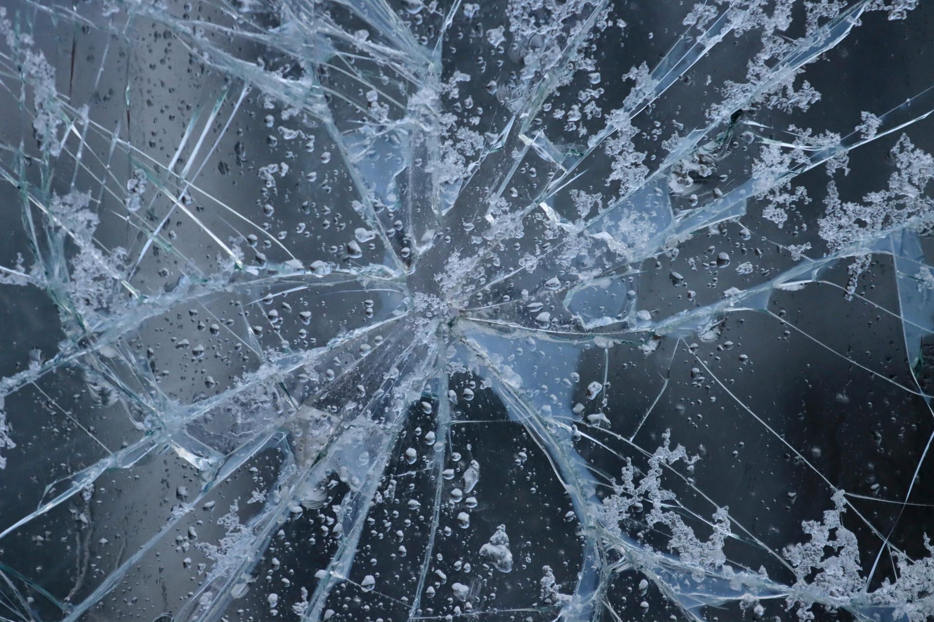 Shattered glass with radiating cracks, ice crystals, and water droplets against a dark background.