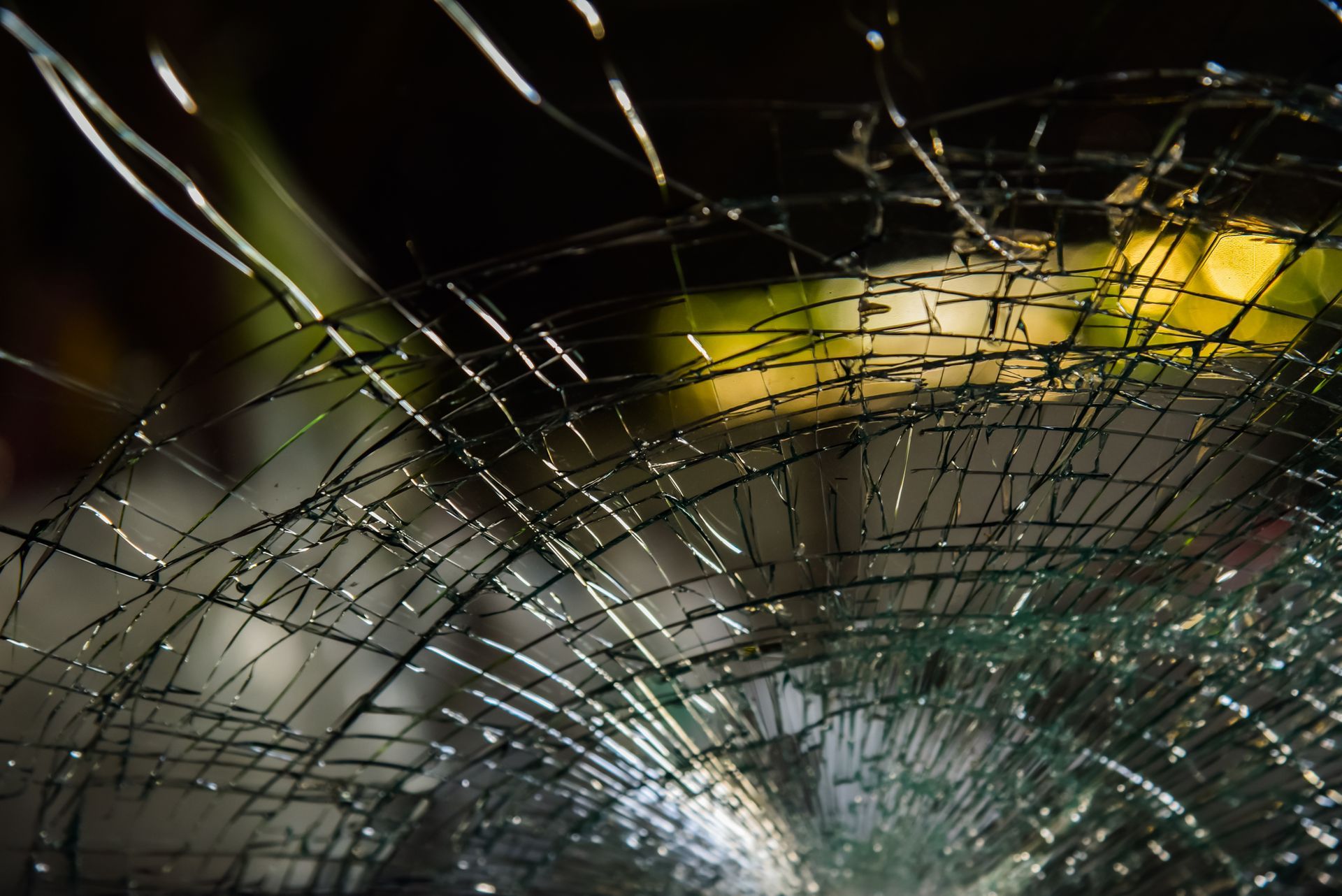 Cracked car windshield with many radiating cracks, blurred background.