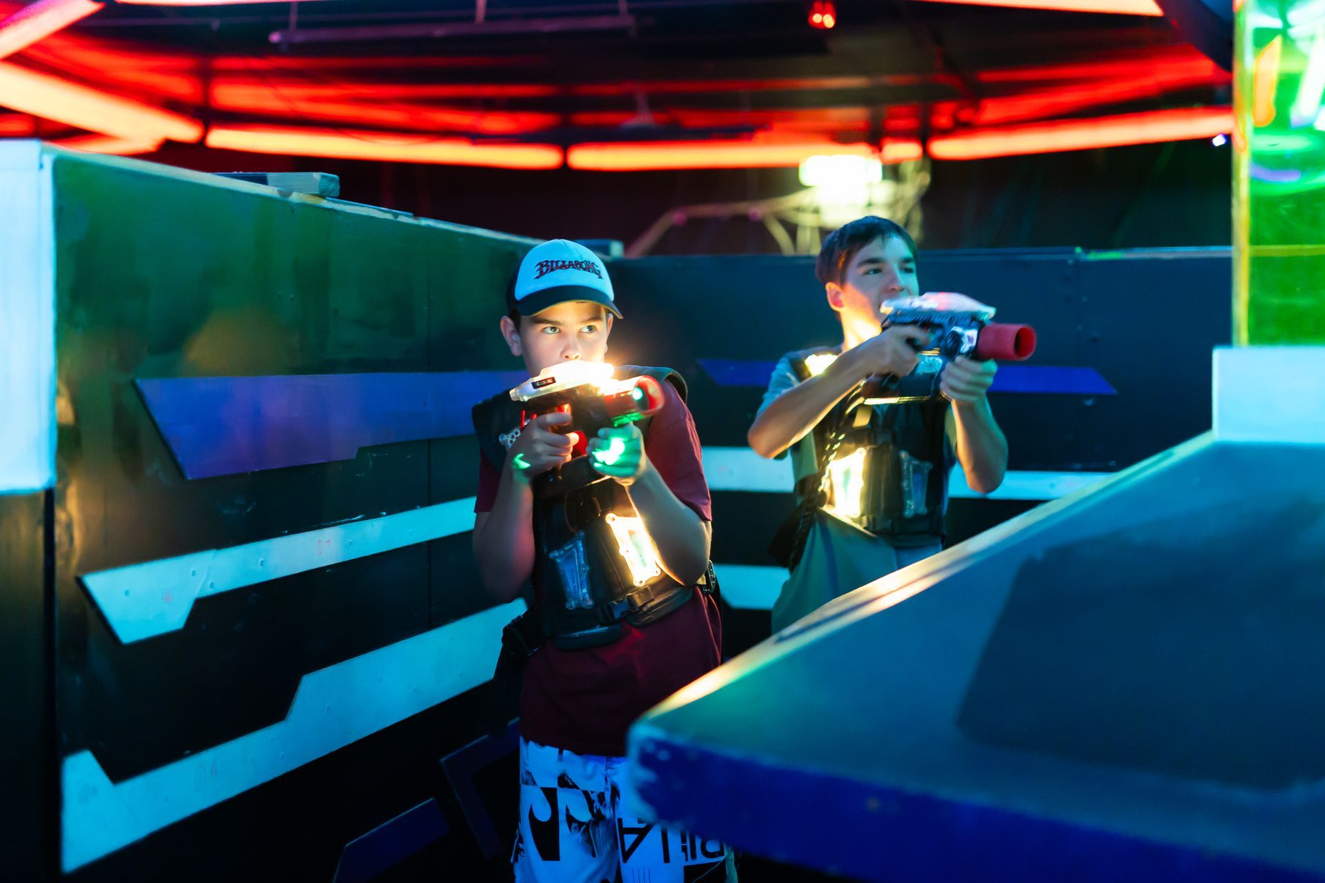 Two people at Laserzone Sunshine Coast playing laser tag in an arena with phasors, wearing vests, and illuminated with colored lights.