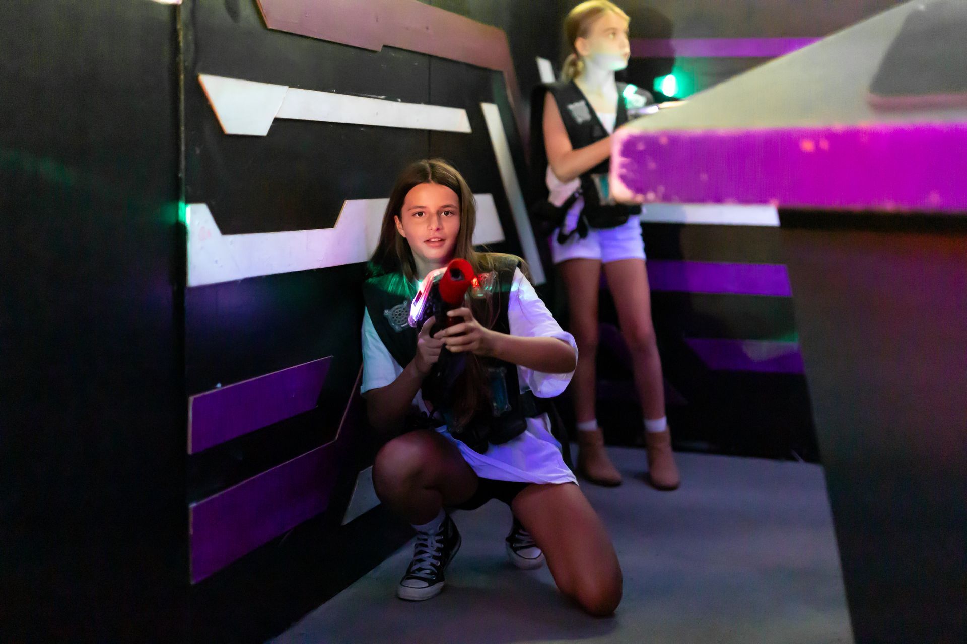 Two people playing laser tag in an arena at Laserzone Sunshine Coast. One is crouching with a laser gun, another stands nearby.