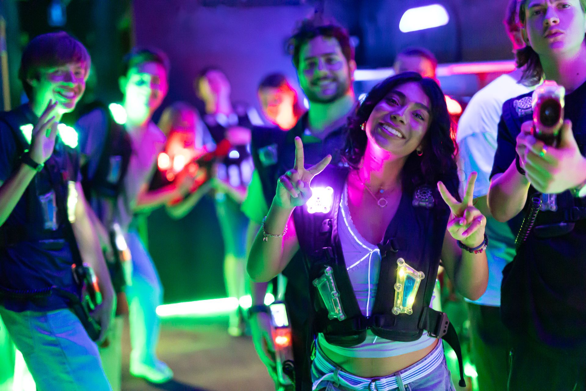 Group of people smiling, posing with laser tag vests in a colorful, illuminated arena.