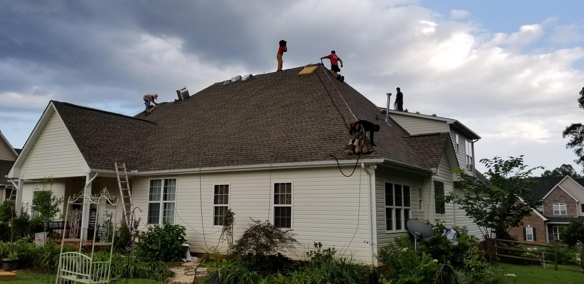 Two men are working on the roof of a white house.