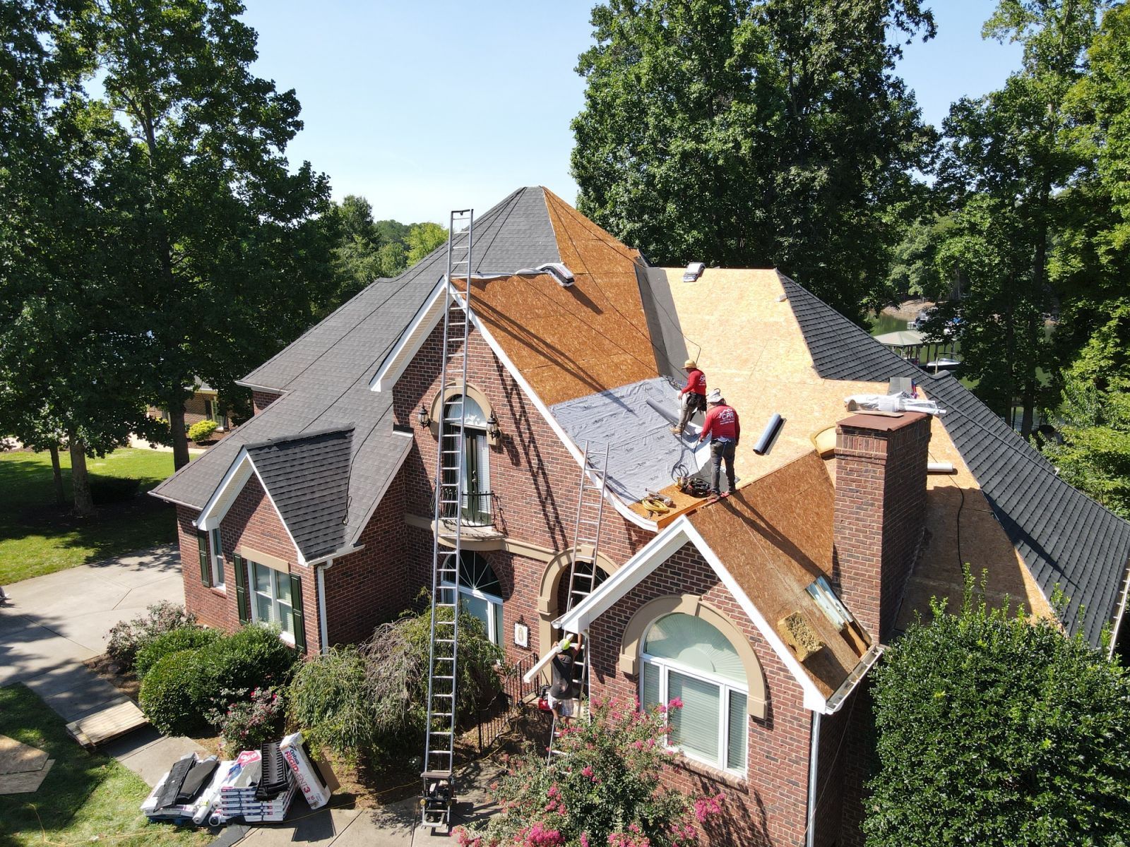 A group of people are working on the roof of a large brick house.