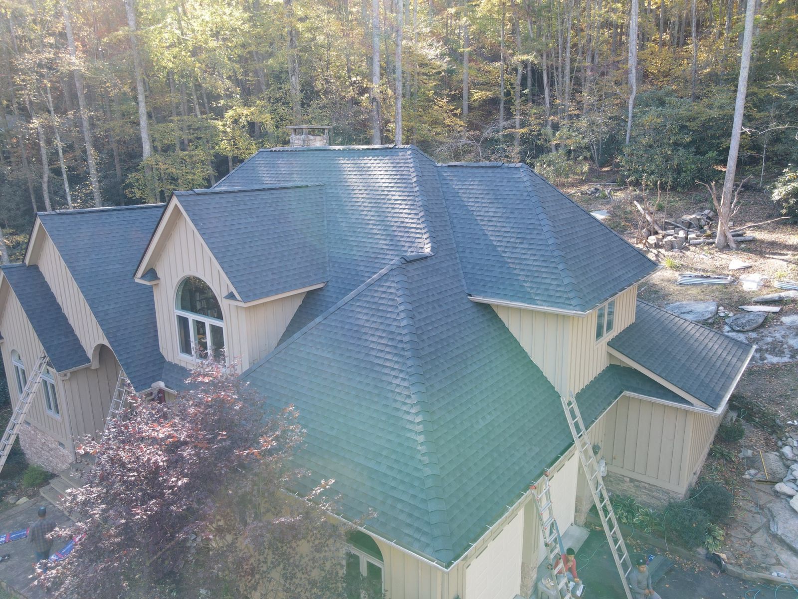 An aerial view of a large house with a black roof surrounded by trees.