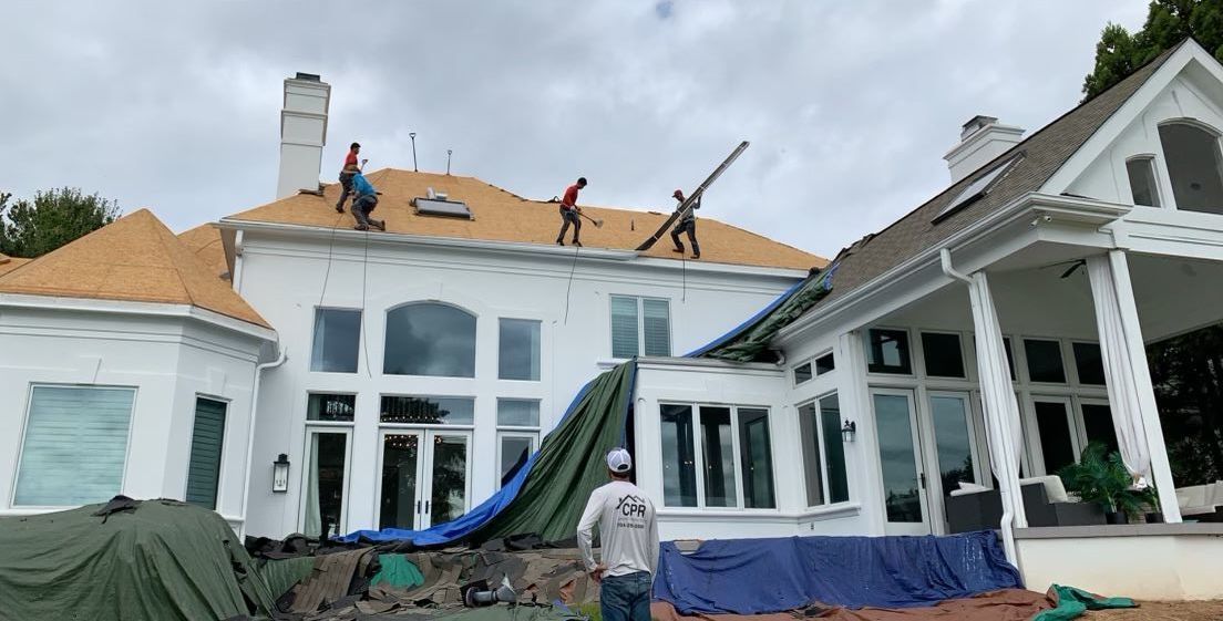 A group of men are working on the roof of a large white house.