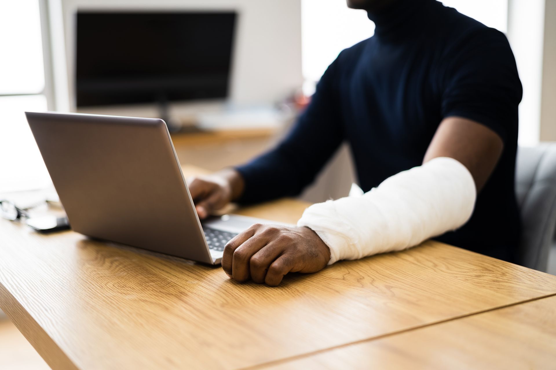 A man with a cast on his arm is using a laptop computer