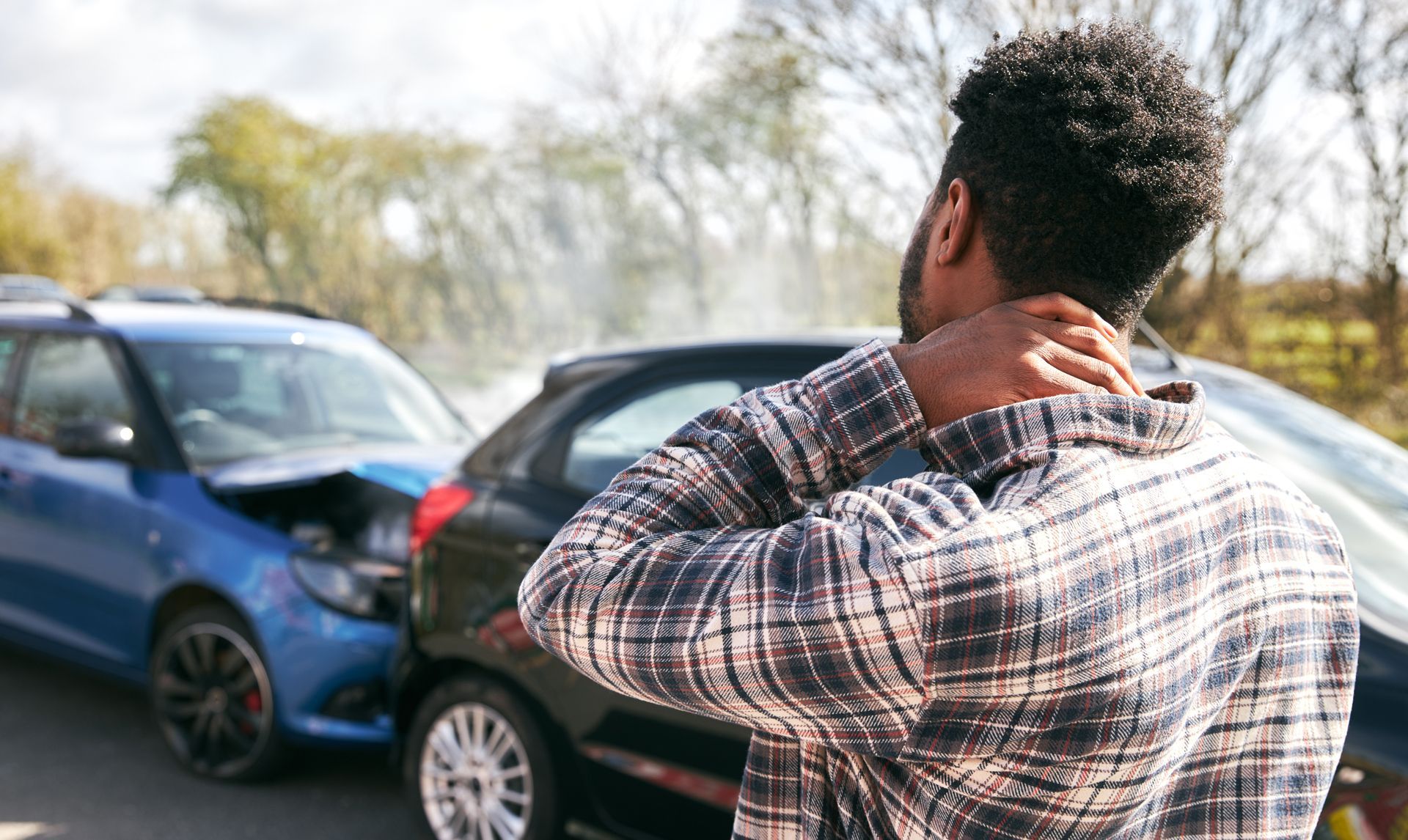 A man is holding his neck in pain in front of a car accident