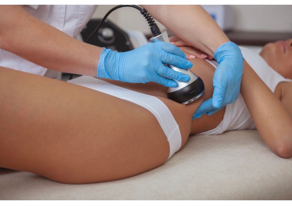 Woman holding a fetal doppler on her belly, forming a heart shape with her hands.