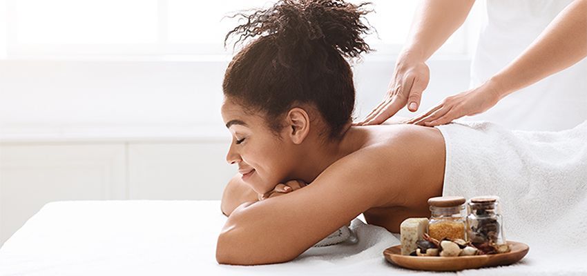 Woman receiving a back massage in a spa, with essential oil bottles and candles.
