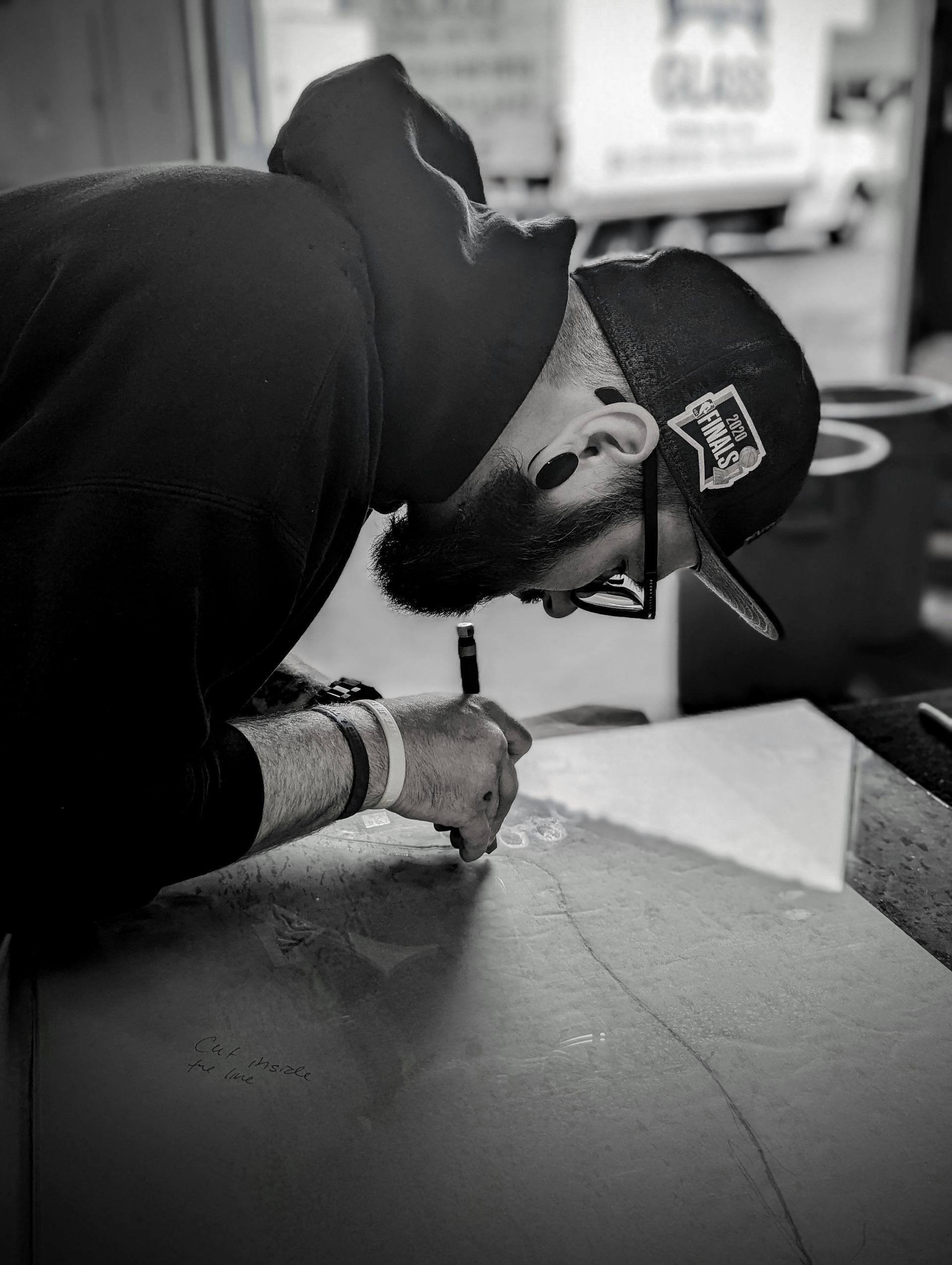 Man with a beard, wearing a hat and hoodie, drawing on a surface with a pen.