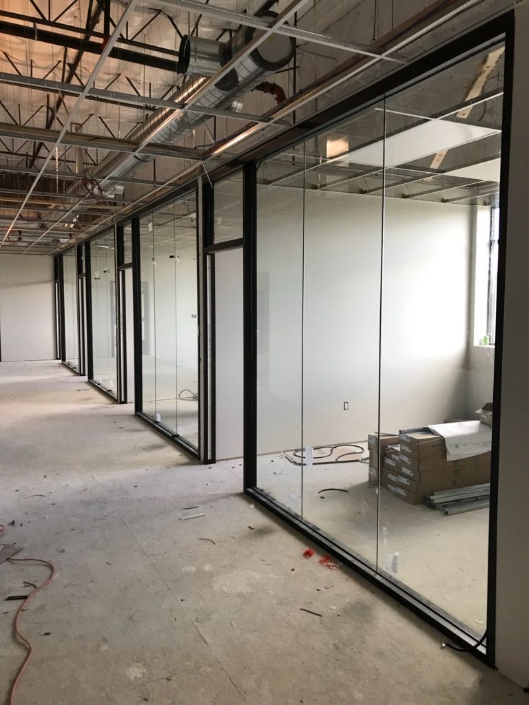 Empty office space with glass-walled rooms under construction; concrete floor, metal ceiling beams.