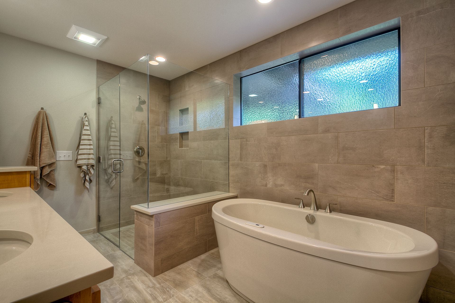Modern bathroom with a glass shower, soaking tub, and window with textured glass.