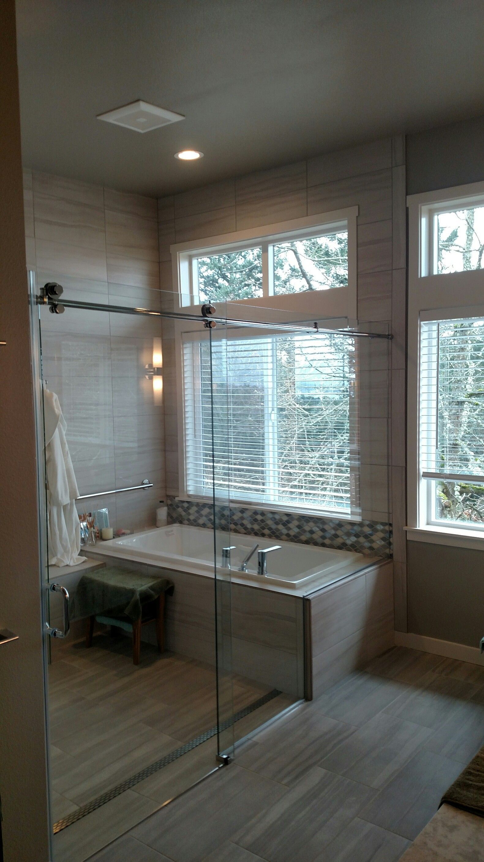 Modern bathroom with glass shower, tub, and large windows with natural light.