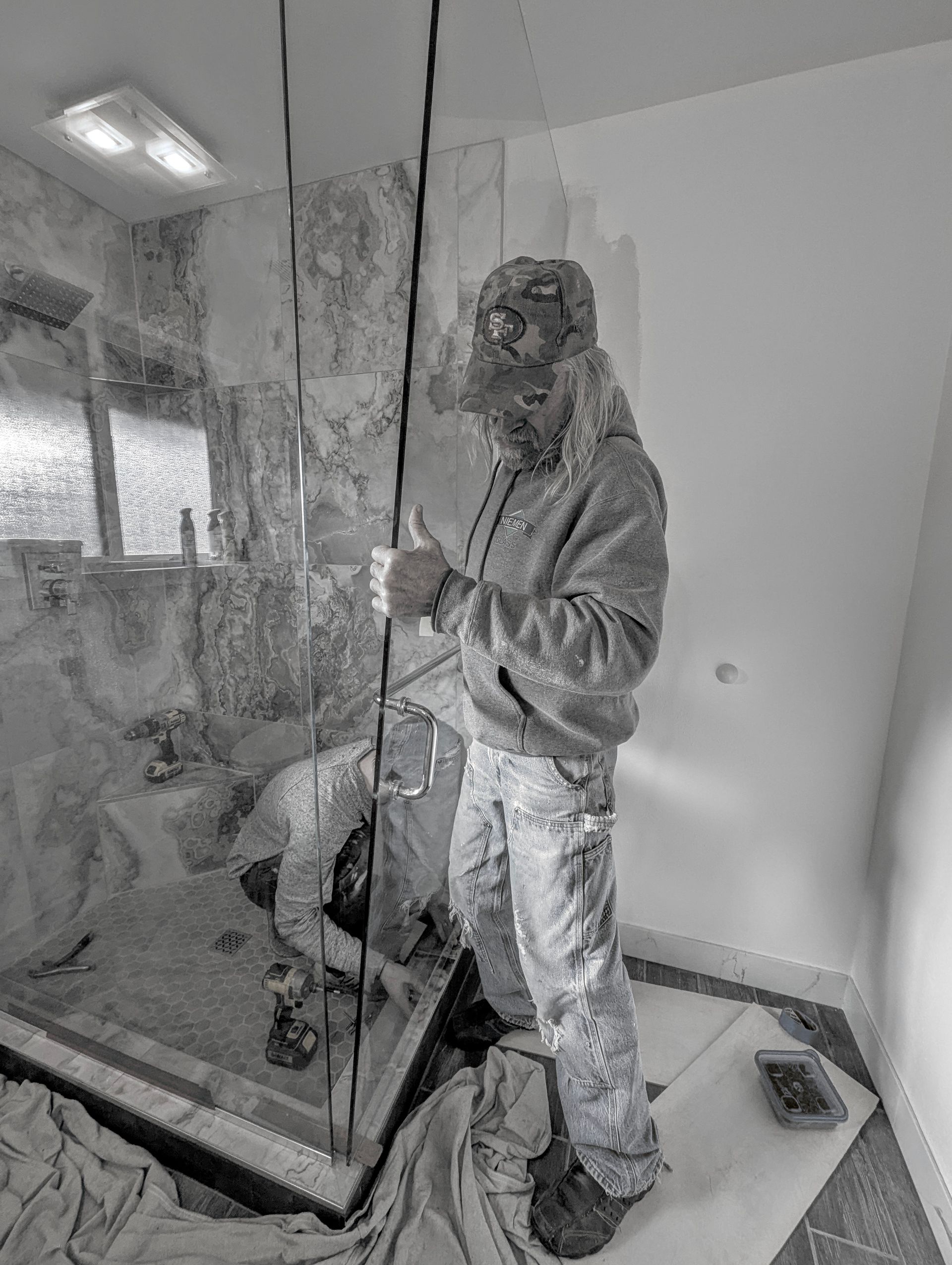 Two people installing glass shower door in bathroom. One stands, another kneels.