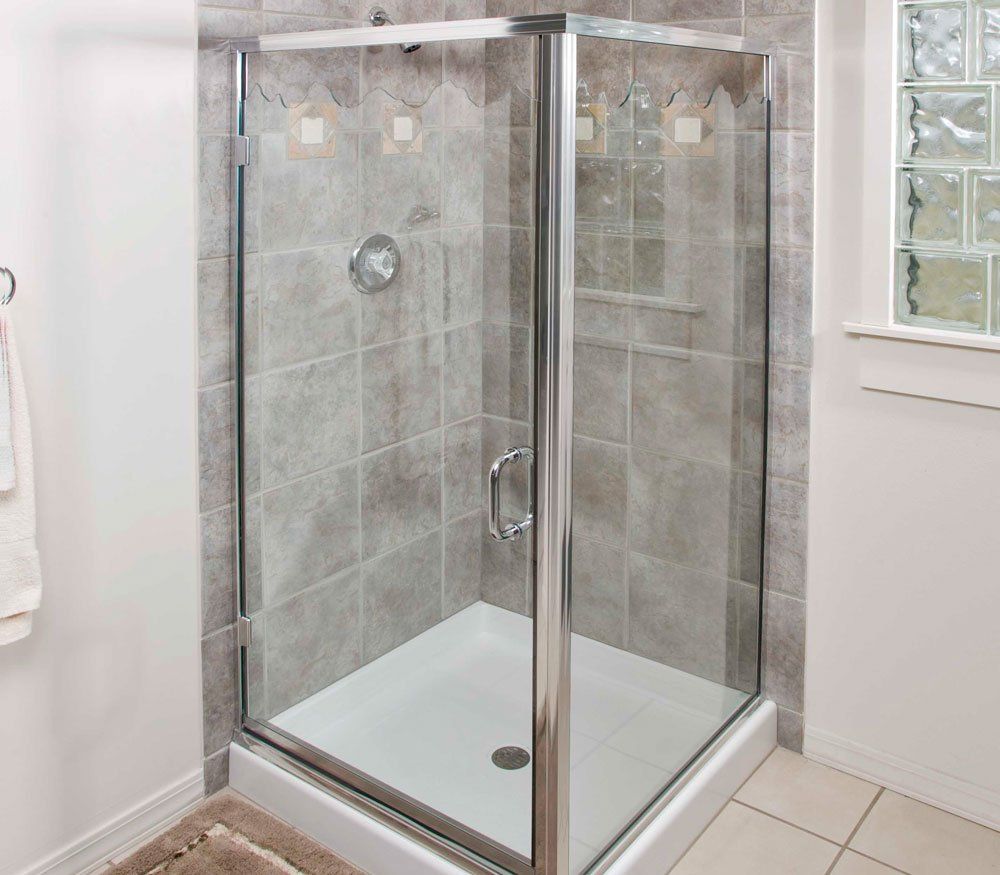 Glass shower enclosure with silver frame, on tiled walls, white base, showerhead, and handle.