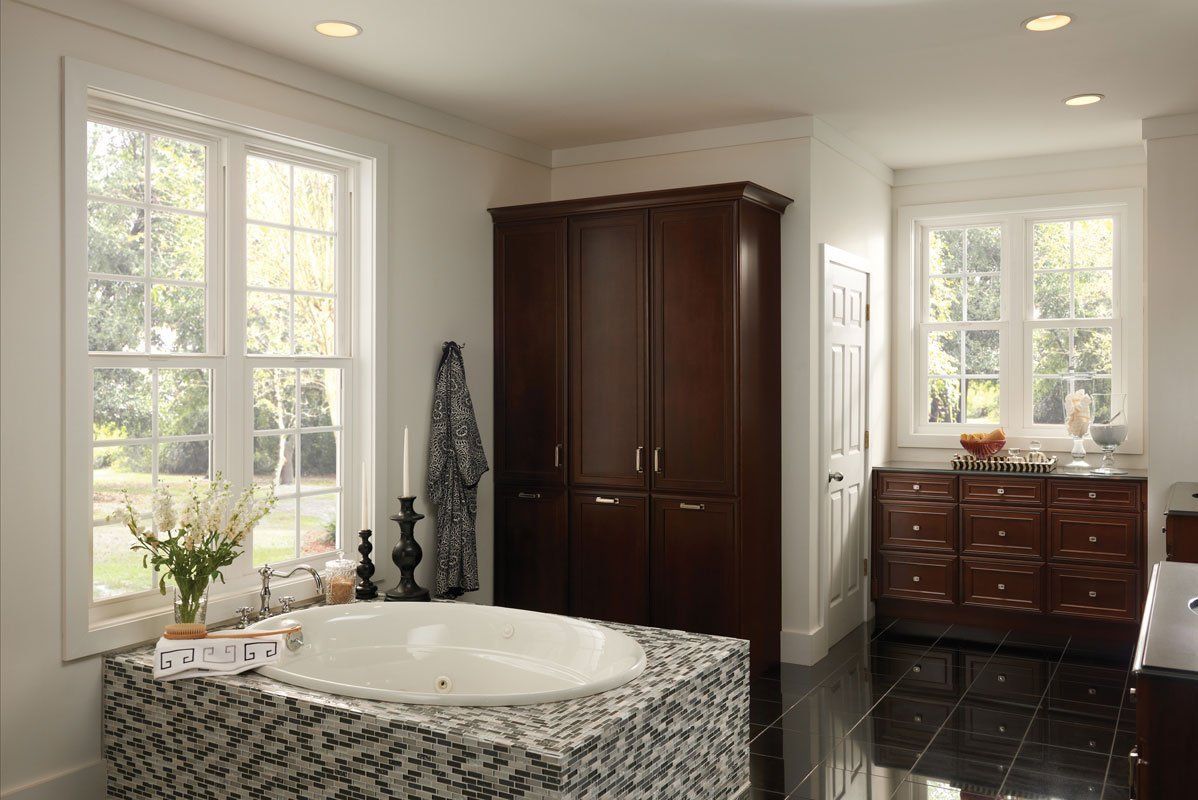 Spacious bathroom with a jacuzzi, dark wood wardrobe, two windows, and dark tiled floor.