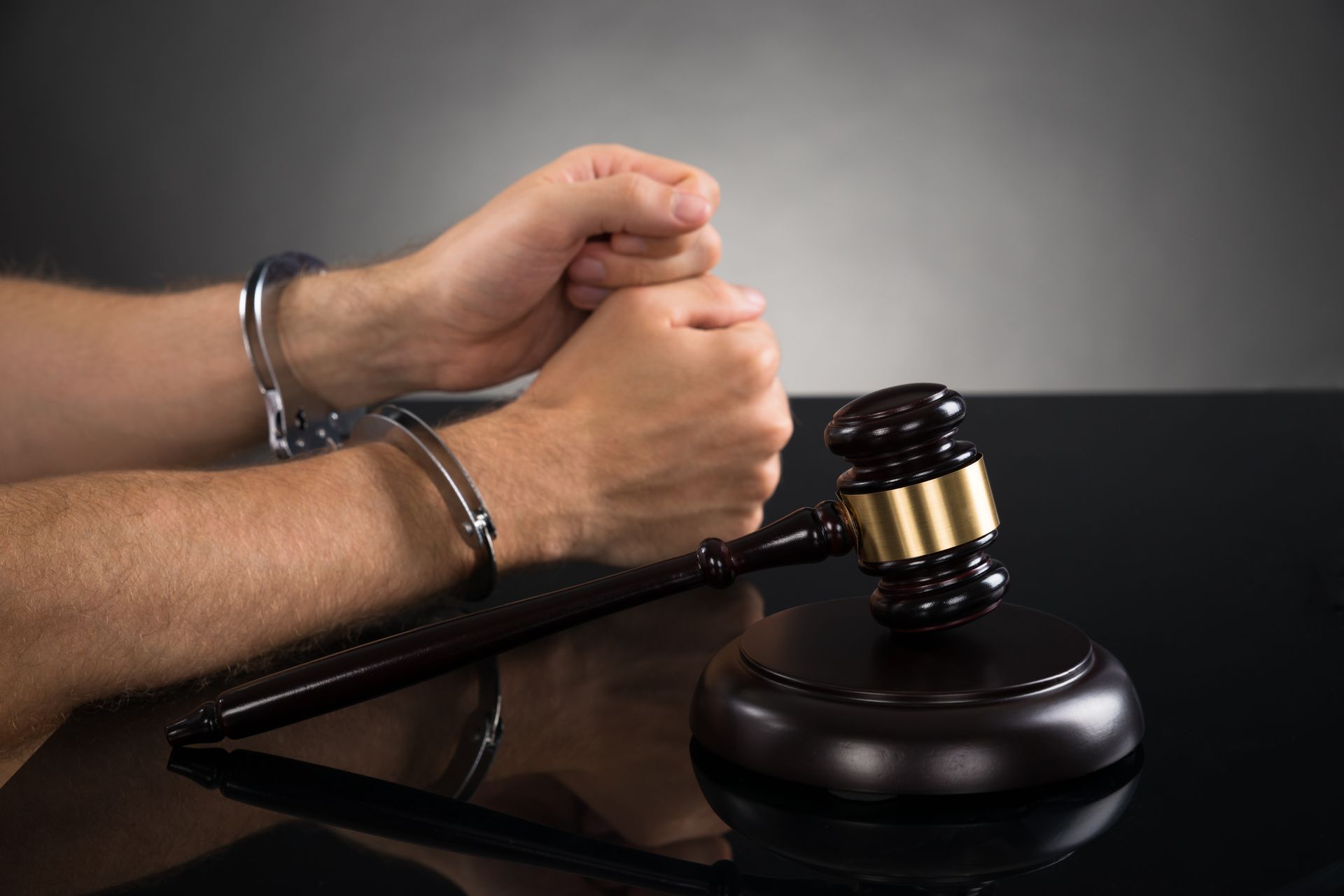 Close-up Of Person Hand In Handcuffs With Gavel At Desk.