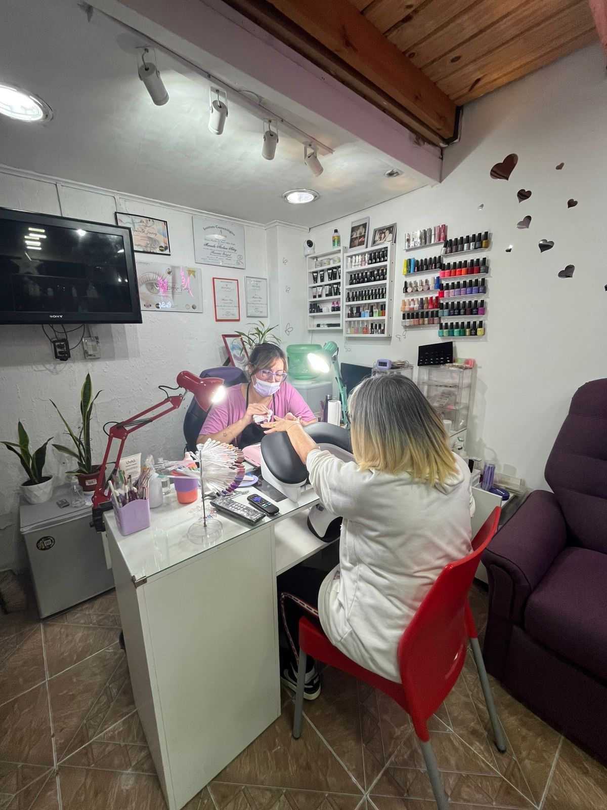 Dos personas sentadas en un puesto de manicura en un pequeño saló