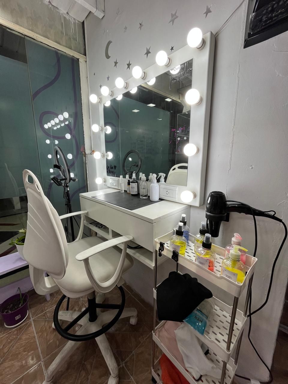 Tocador con espejo iluminado, silla blanca y cosméticos sobre una mesa pequeña en una habitación gris.