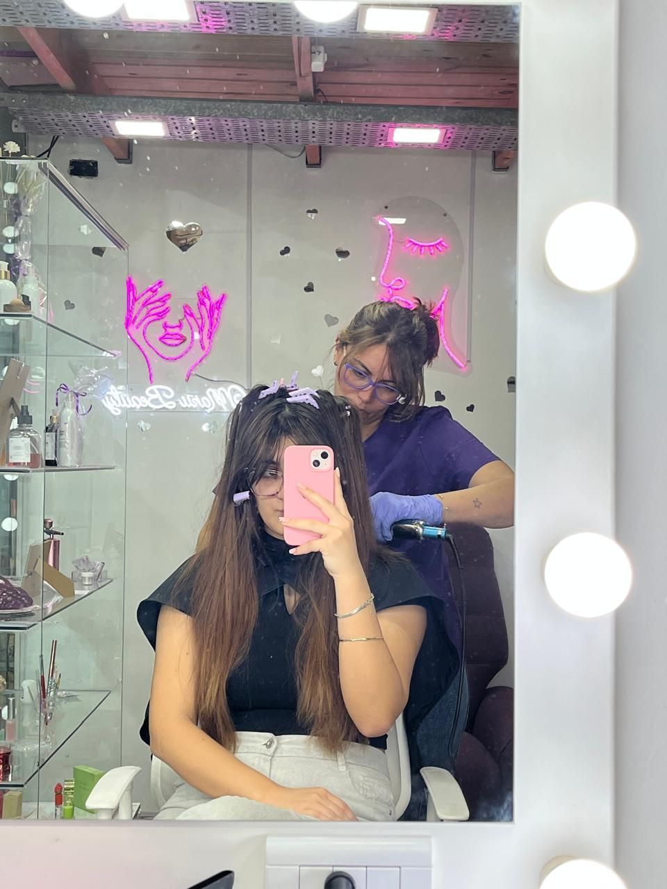 Una persona se toma una selfie frente al espejo en una peluquería mientras un estilista le arregla el cabello.