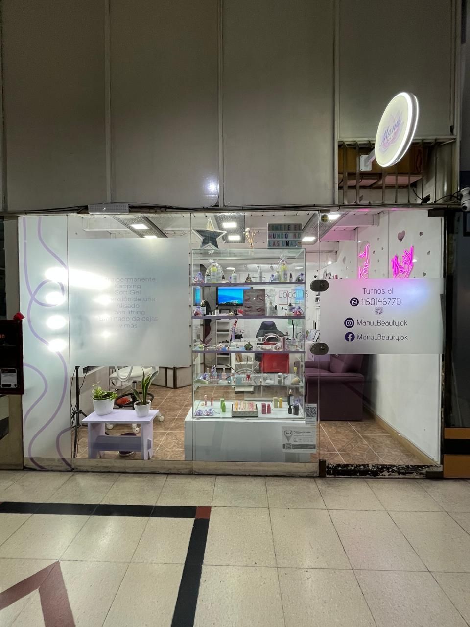 Pequeño quiosco comercial con estantes, productos y luces brillantes en el pasillo de un centro comercial.