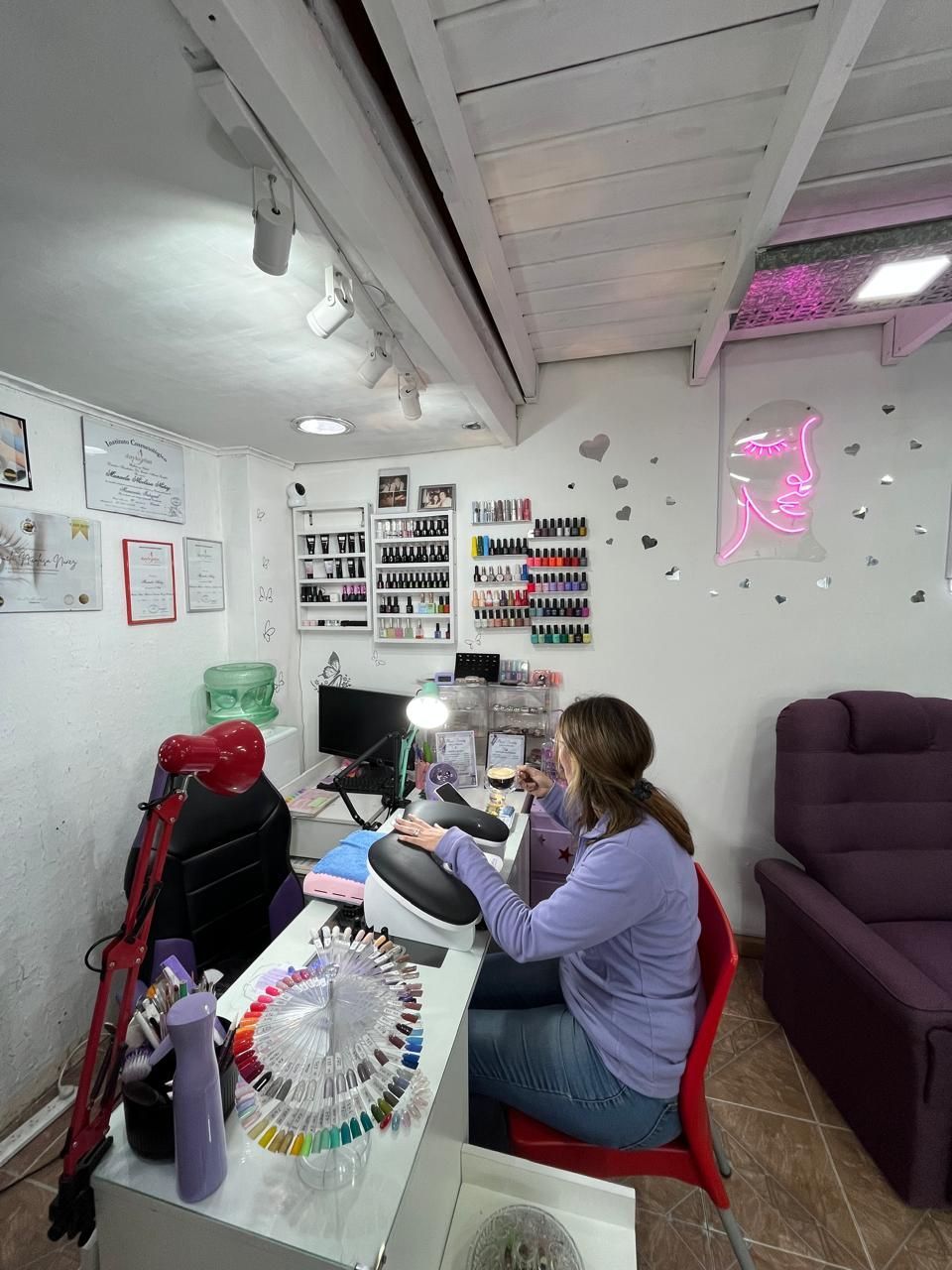 Una persona cose en un escritorio en una pequeña sala de manualidades con hilo, tela y estantes llenos de materiales.