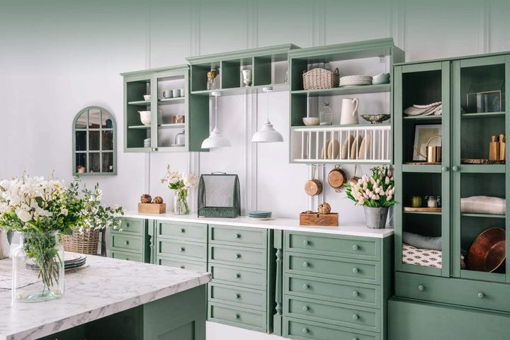 A kitchen with green cabinets and a vase of flowers on the counter.