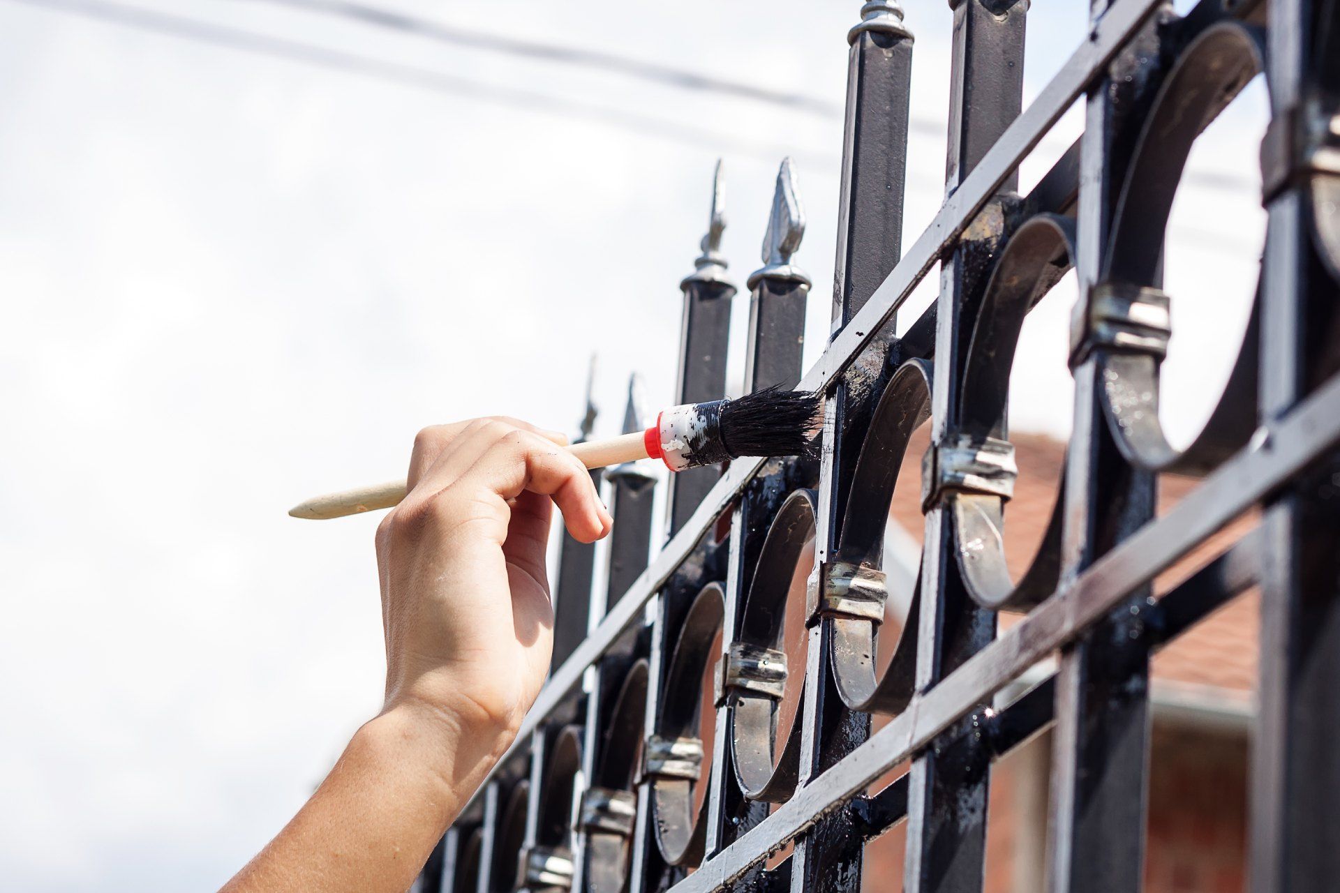 A person is painting a wrought iron fence with a brush.