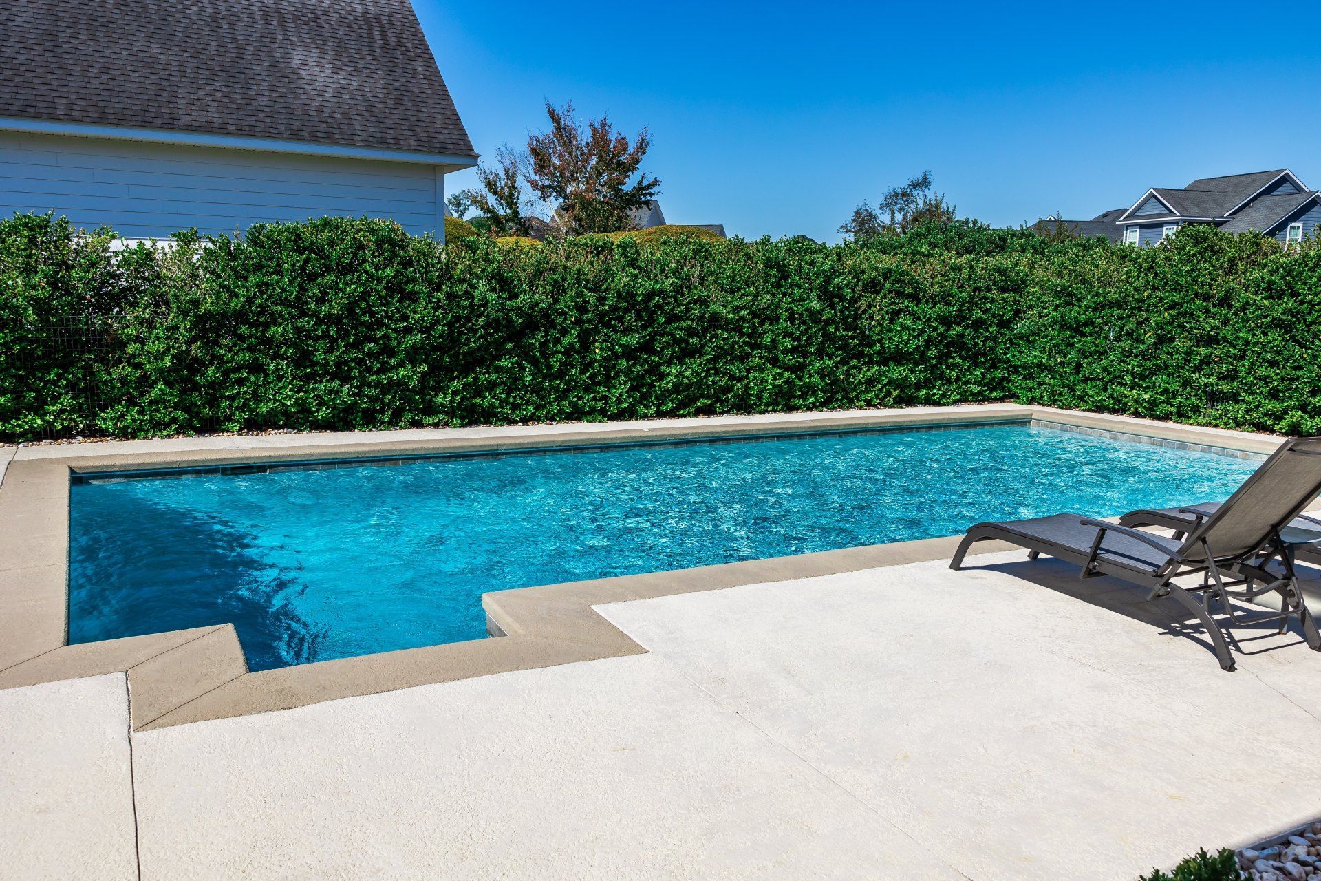 A large swimming pool is surrounded by chairs and a hedge.
