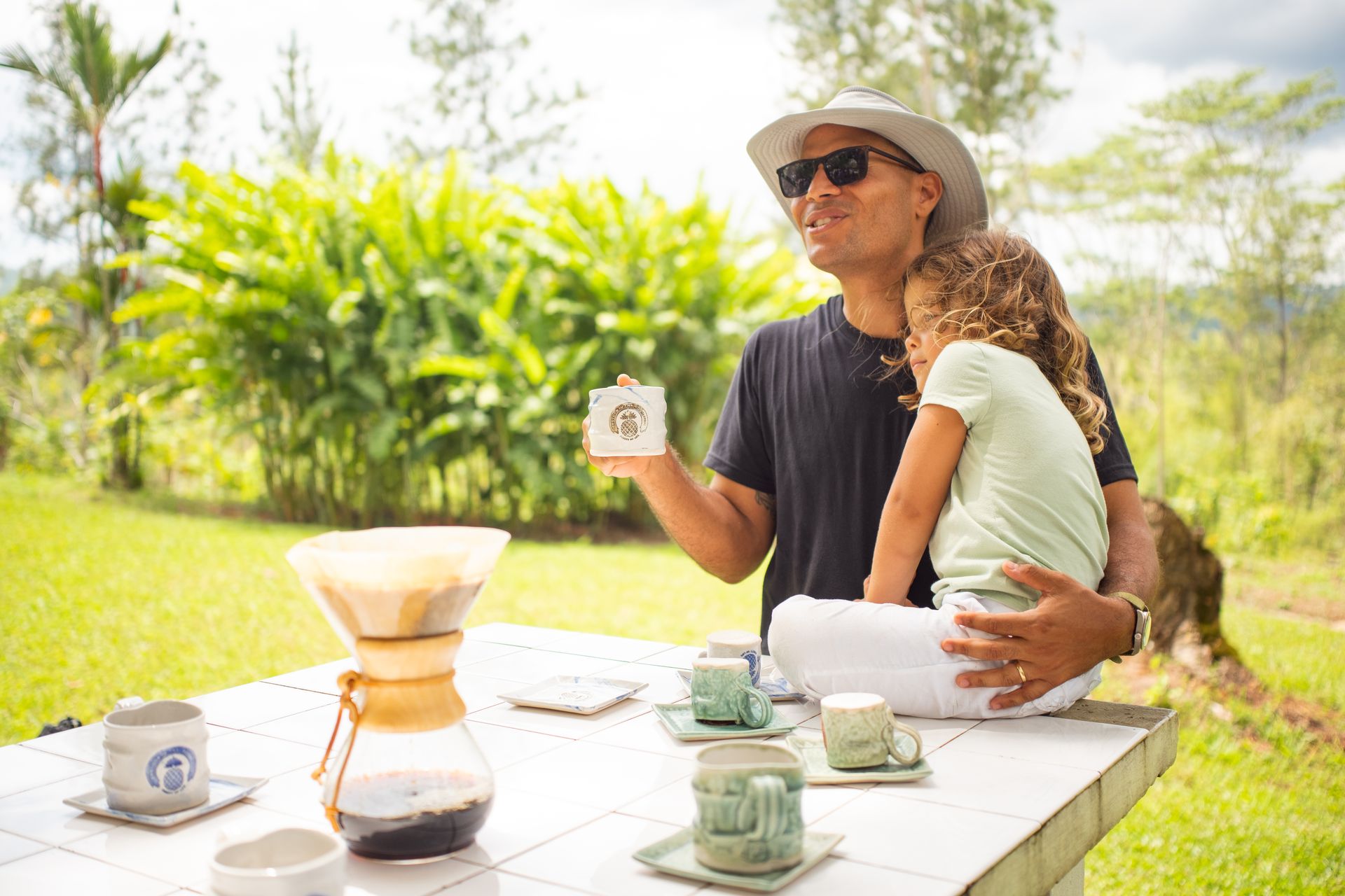 A man is holding a child while sitting at a table holding a cup of coffee.