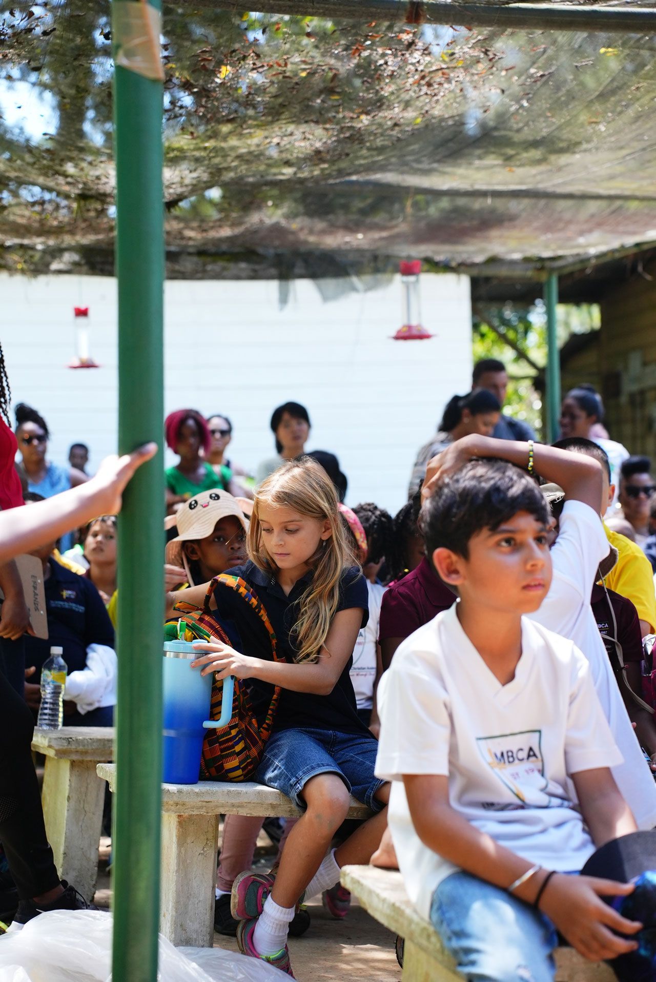 A group of children are sitting on benches under a canopy