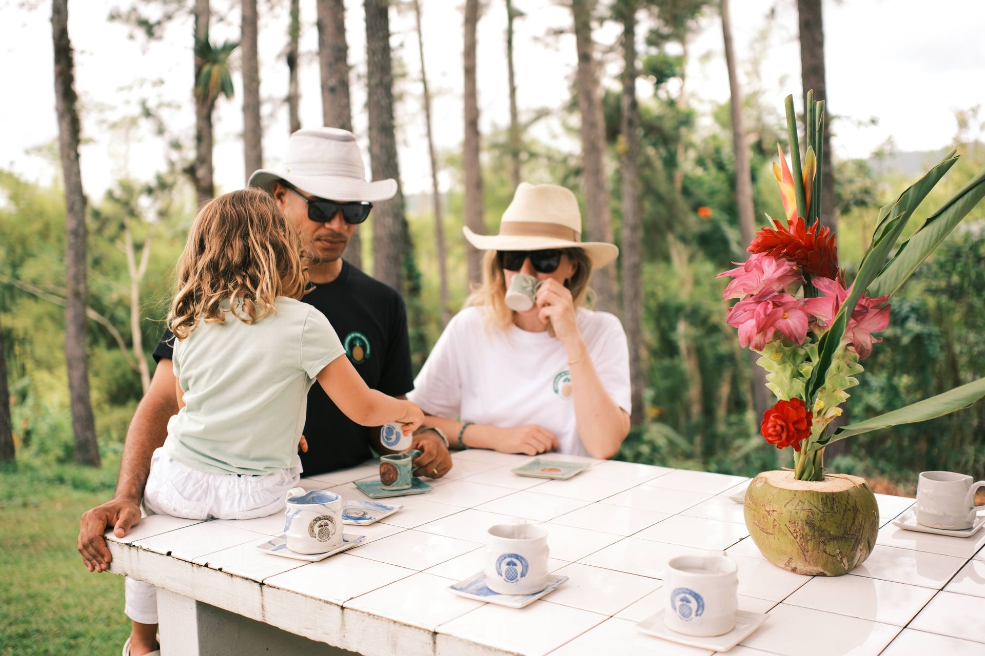 A family is sitting at a table in the woods drinking coffee